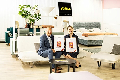 2 Personen sitzen auf einem Sofa und präsentieren stolz die Urkunde ©JOKA Kapsamer GmbH